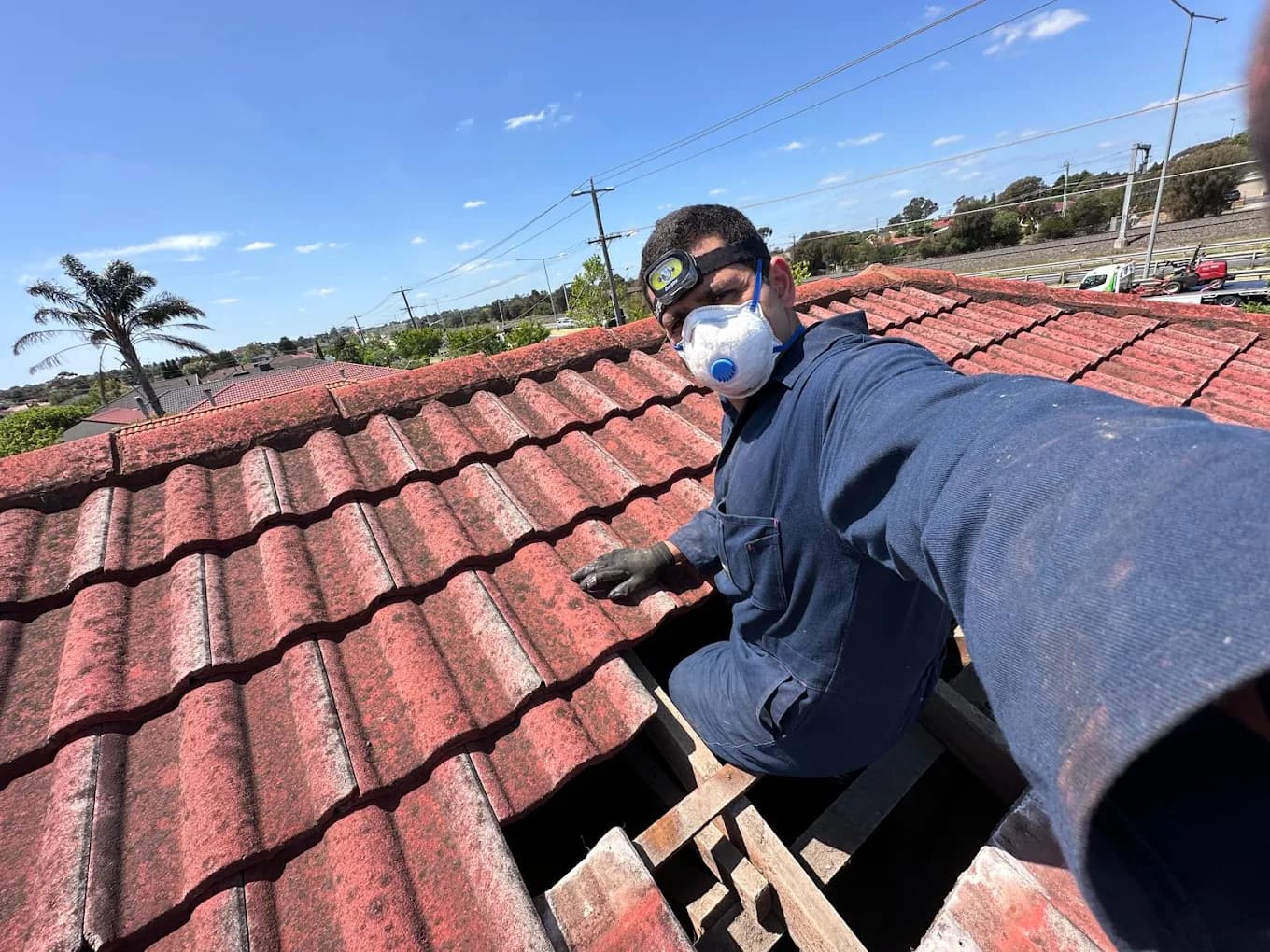 Mark working in a roof cavity on a tiled Melbourne roof, wearing a head torch and dust mask